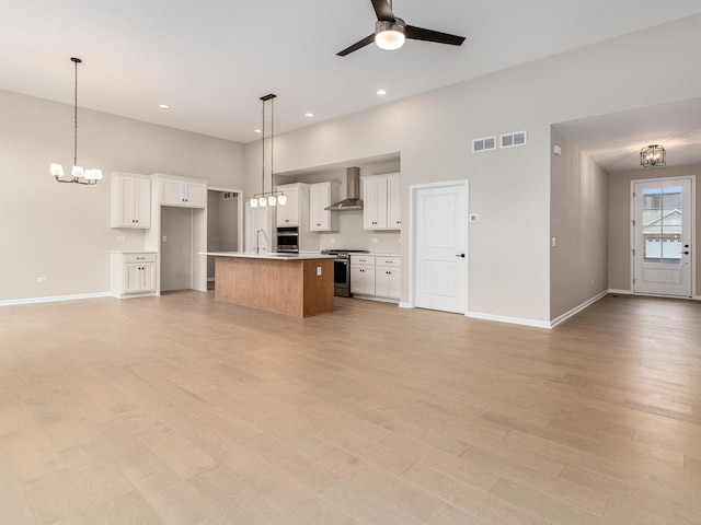 kitchen with appliances with stainless steel finishes, white cabinetry, decorative light fixtures, an island with sink, and wall chimney exhaust hood