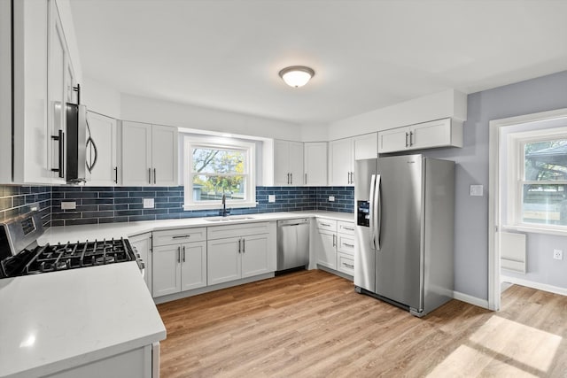 kitchen featuring light wood-type flooring, tasteful backsplash, stainless steel appliances, sink, and white cabinets