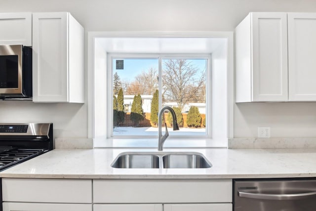 kitchen with light stone counters, stainless steel appliances, white cabinetry, and sink