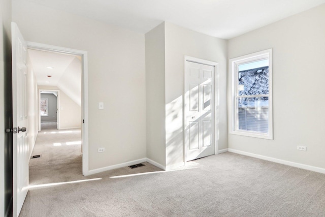 interior space featuring multiple windows, vaulted ceiling, light carpet, and a closet