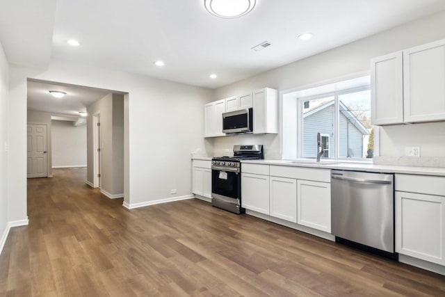 kitchen with appliances with stainless steel finishes, dark hardwood / wood-style floors, white cabinets, and sink