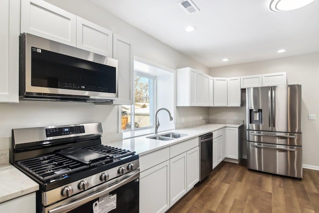 kitchen with appliances with stainless steel finishes, light stone countertops, dark hardwood / wood-style flooring, sink, and white cabinetry