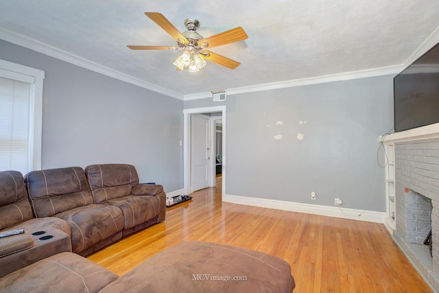 living room with light wood-type flooring, a brick fireplace, a textured ceiling, ceiling fan, and crown molding