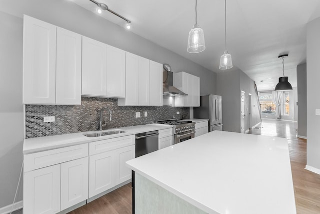 kitchen with a center island, wall chimney range hood, sink, appliances with stainless steel finishes, and white cabinetry