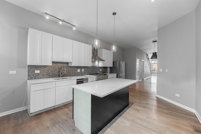 kitchen featuring pendant lighting, white cabinets, sink, wall chimney exhaust hood, and stainless steel appliances