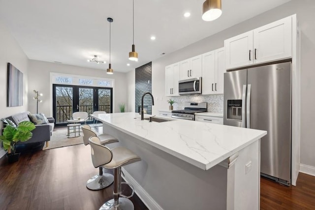 kitchen with light stone countertops, sink, pendant lighting, a kitchen island with sink, and appliances with stainless steel finishes