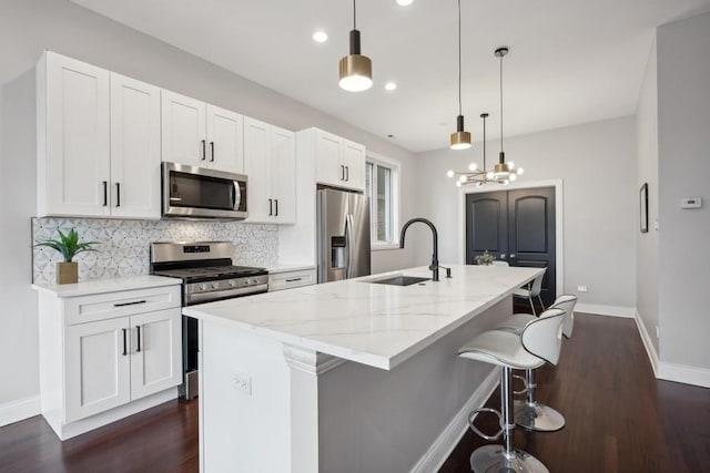 kitchen featuring light stone counters, stainless steel appliances, sink, decorative light fixtures, and an island with sink