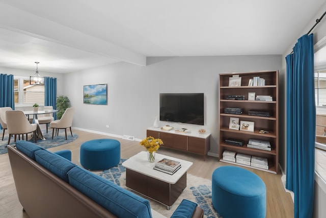 living room featuring vaulted ceiling with beams, a chandelier, and light wood-type flooring