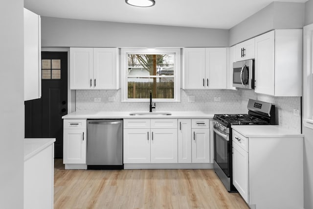 kitchen featuring backsplash, sink, appliances with stainless steel finishes, light hardwood / wood-style floors, and white cabinetry