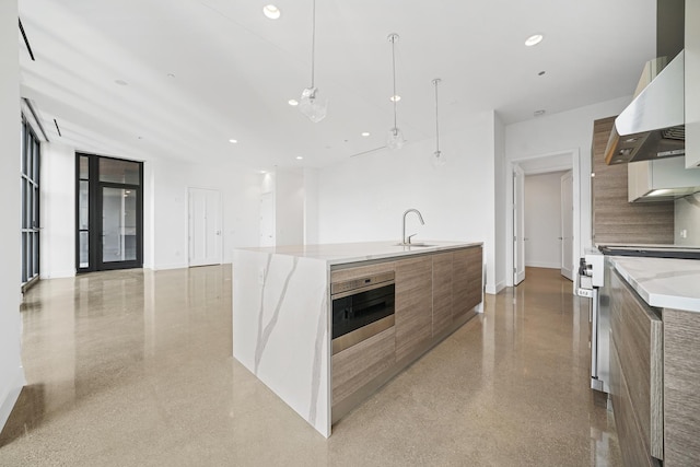 kitchen with sink, wall chimney exhaust hood, a large island with sink, pendant lighting, and appliances with stainless steel finishes