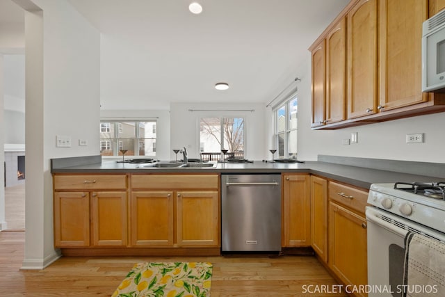 kitchen featuring light wood-type flooring, white appliances, sink, and a tile fireplace