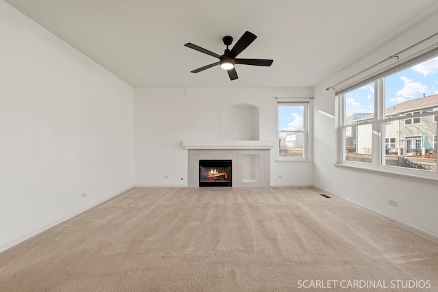 unfurnished living room with ceiling fan, light carpet, and a tiled fireplace