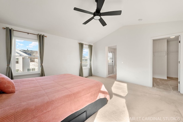 bedroom with lofted ceiling, a walk in closet, ensuite bath, ceiling fan, and light colored carpet