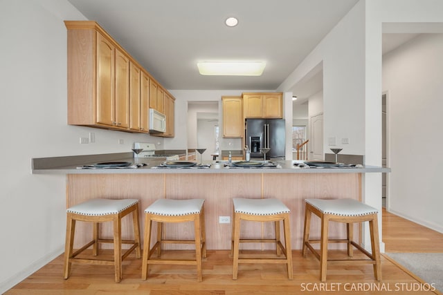 kitchen with light wood-type flooring, stainless steel fridge with ice dispenser, stove, and light brown cabinets