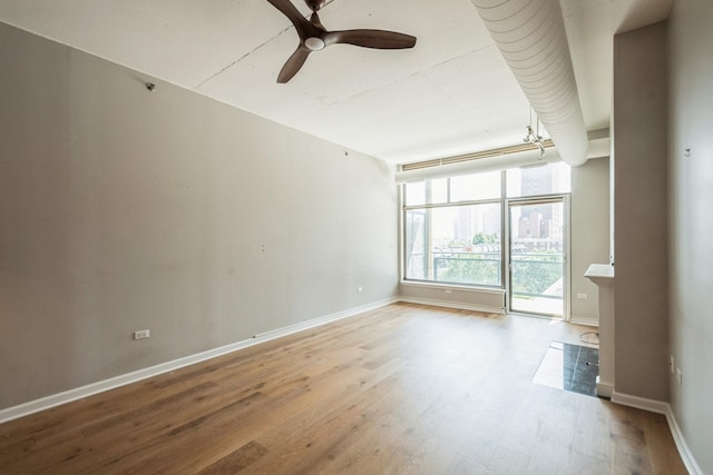 unfurnished room with ceiling fan, expansive windows, baseboards, and wood finished floors