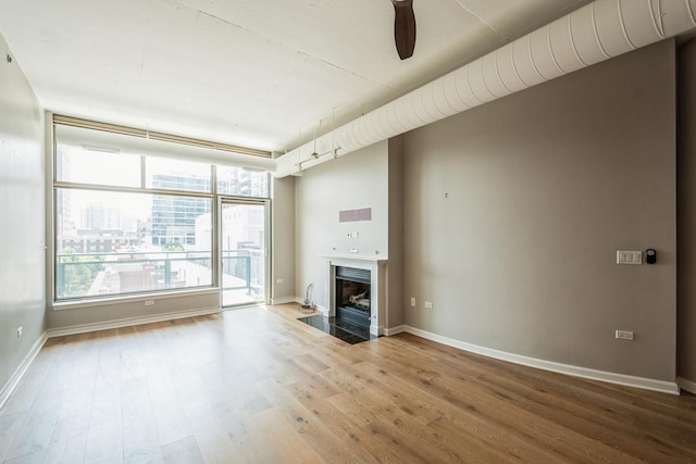 unfurnished living room with a fireplace with flush hearth, baseboards, a city view, and wood finished floors