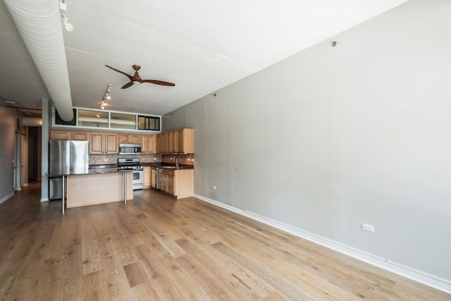 kitchen featuring stainless steel appliances, a sink, a kitchen island, open floor plan, and tasteful backsplash