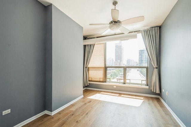 empty room featuring light wood-style floors, a city view, ceiling fan, and baseboards