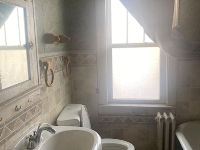 bathroom with sink, toilet, tile walls, radiator heating unit, and a tub