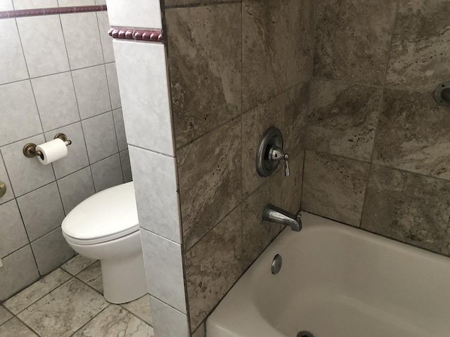 bathroom featuring toilet, tub / shower combination, and tile walls