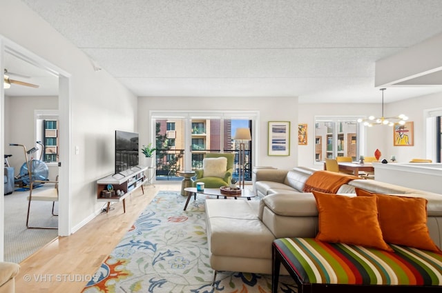 living room with a textured ceiling, light hardwood / wood-style floors, and ceiling fan with notable chandelier