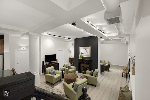 living room featuring a large fireplace, decorative columns, light hardwood / wood-style flooring, and track lighting