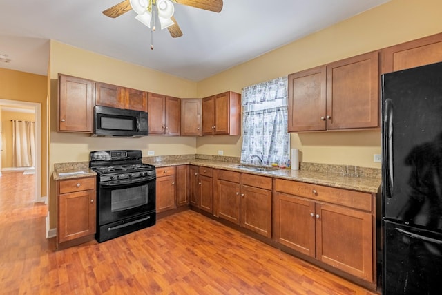 kitchen with black appliances, sink, light hardwood / wood-style flooring, ceiling fan, and light stone countertops