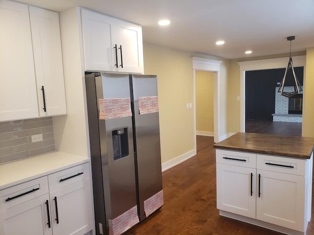 kitchen with white cabinetry, a brick fireplace, dark wood-type flooring, backsplash, and stainless steel fridge