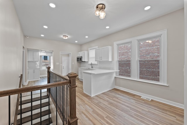 kitchen with sink, white cabinetry, light wood-type flooring, kitchen peninsula, and decorative backsplash