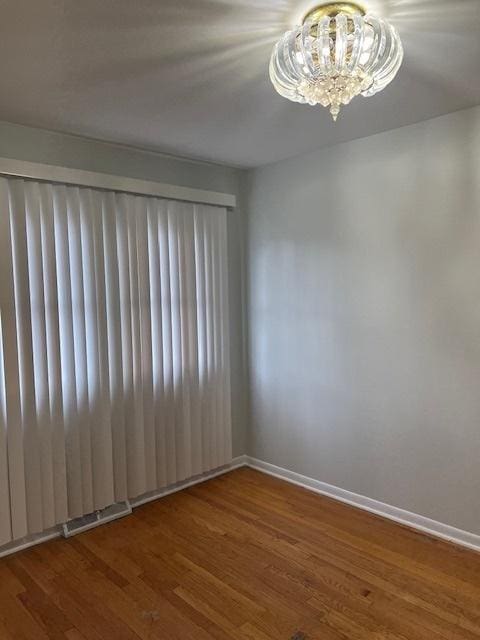 empty room with hardwood / wood-style floors and a chandelier