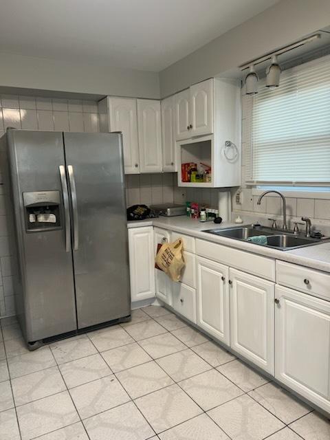 kitchen with decorative backsplash, stainless steel fridge, white cabinetry, and sink