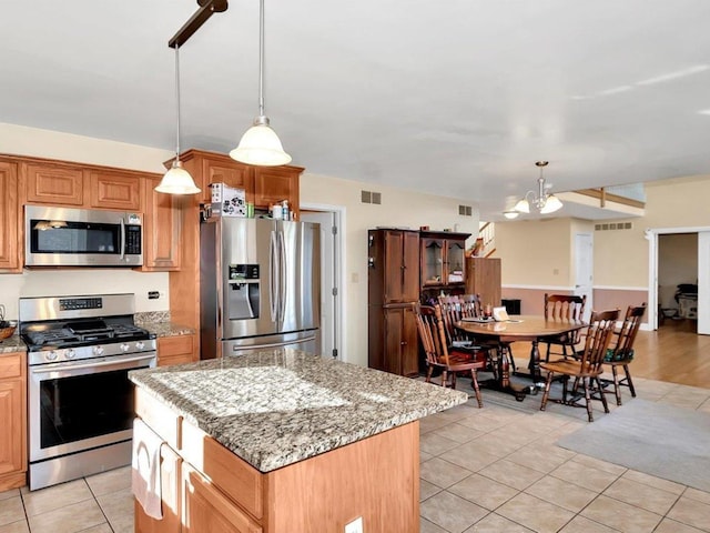 kitchen with appliances with stainless steel finishes, light stone counters, light tile patterned floors, an inviting chandelier, and a center island