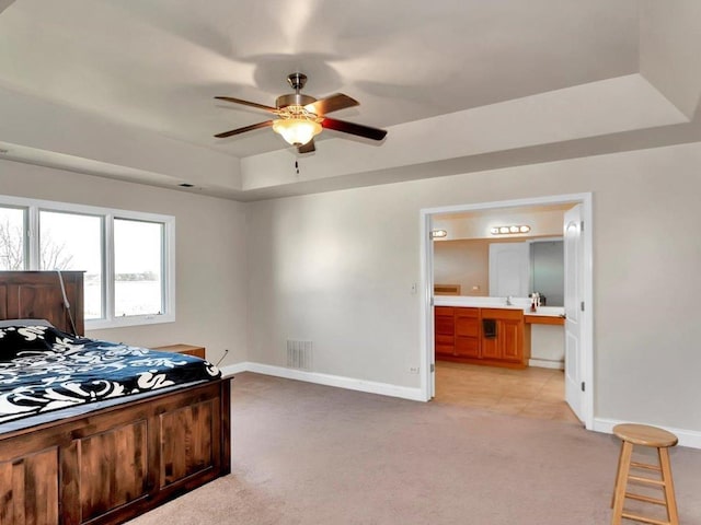 bedroom with a tray ceiling, ensuite bathroom, ceiling fan, and light colored carpet