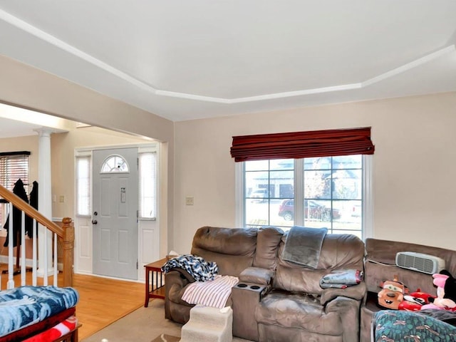 living room featuring a tray ceiling, decorative columns, and light wood-type flooring