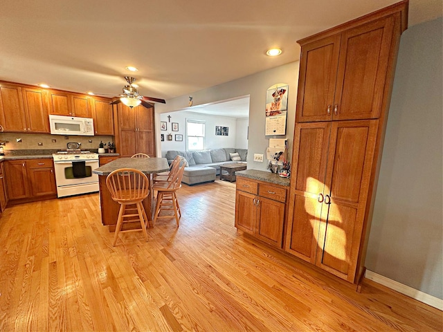 kitchen featuring ceiling fan, light hardwood / wood-style flooring, backsplash, white appliances, and a kitchen bar