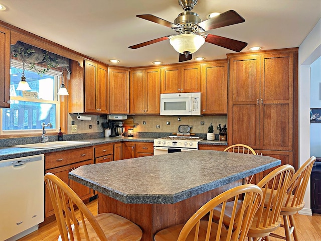 kitchen with white appliances, a kitchen breakfast bar, sink, ceiling fan, and light wood-type flooring