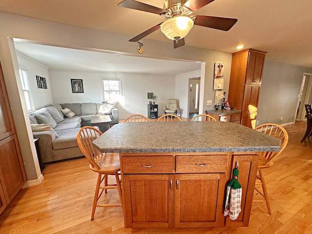 kitchen with light wood-type flooring, a center island, ceiling fan, and a breakfast bar area