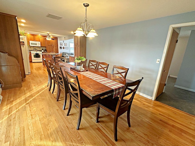 dining space featuring ceiling fan with notable chandelier and light hardwood / wood-style floors