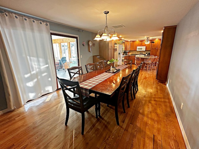 dining space with ceiling fan with notable chandelier and light wood-type flooring