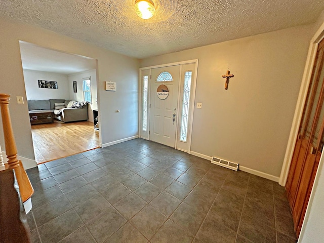 foyer featuring a textured ceiling, dark tile patterned floors, and plenty of natural light