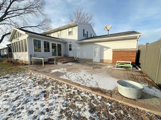 snow covered rear of property with a sunroom and a patio