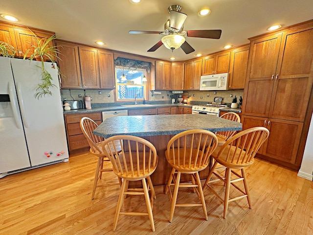 kitchen featuring sink, a kitchen breakfast bar, light hardwood / wood-style flooring, white appliances, and a kitchen island