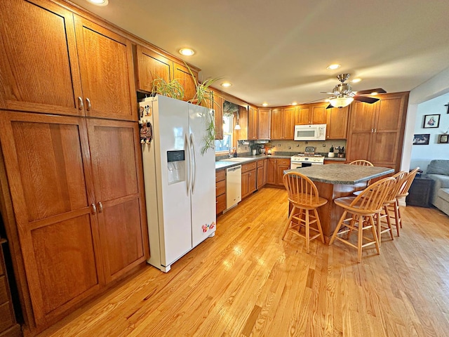 kitchen featuring ceiling fan, a center island, light hardwood / wood-style floors, white appliances, and a kitchen bar