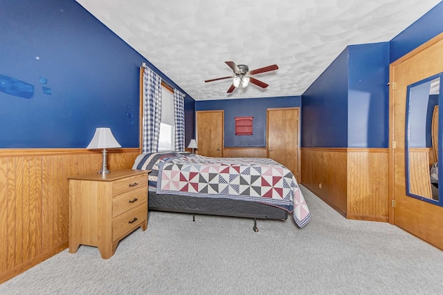 carpeted bedroom with ceiling fan, a textured ceiling, and wood walls