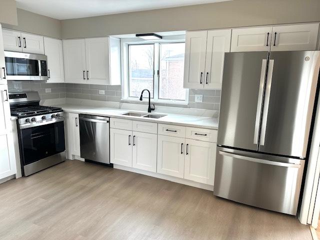 kitchen with sink, stainless steel appliances, light hardwood / wood-style flooring, decorative backsplash, and white cabinets