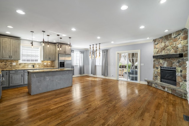 kitchen with dark wood-type flooring, stainless steel refrigerator with ice dispenser, decorative backsplash, decorative light fixtures, and a kitchen island