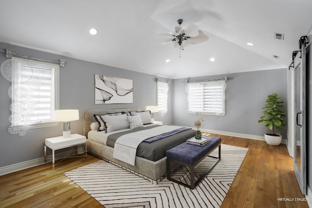 bedroom featuring a barn door, ceiling fan, light hardwood / wood-style flooring, and lofted ceiling