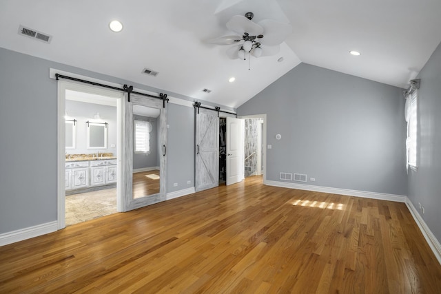 unfurnished bedroom featuring ensuite bathroom, vaulted ceiling, ceiling fan, a barn door, and hardwood / wood-style floors