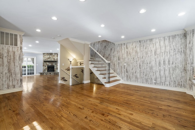 unfurnished living room with a stone fireplace, wood-type flooring, and ornamental molding