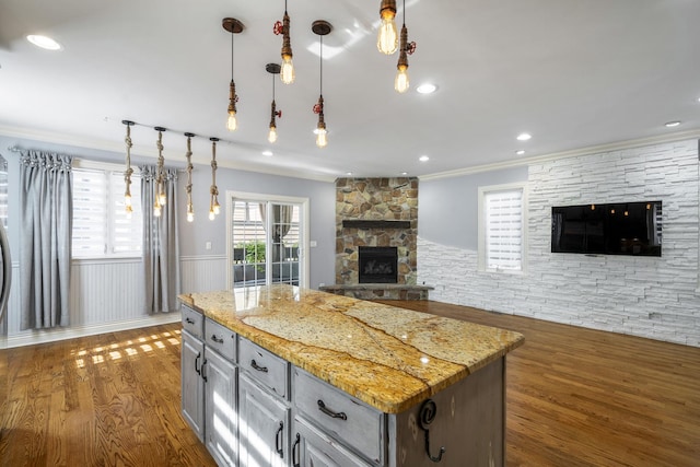 kitchen featuring a fireplace, light stone countertops, a center island, and dark wood-type flooring